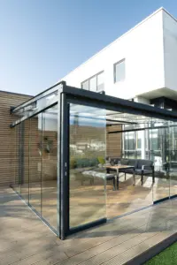 Moderne Terrasse mit Glasüberdachung, Sitzbereich und weißer Gebäudefassade im Hintergrund.